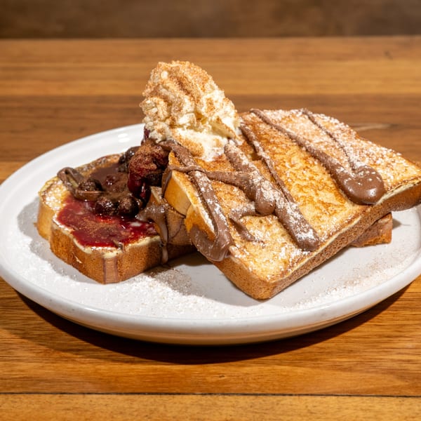 French toast slices topped with whipped cream, chocolate drizzle, powdered sugar, and fruit compote.