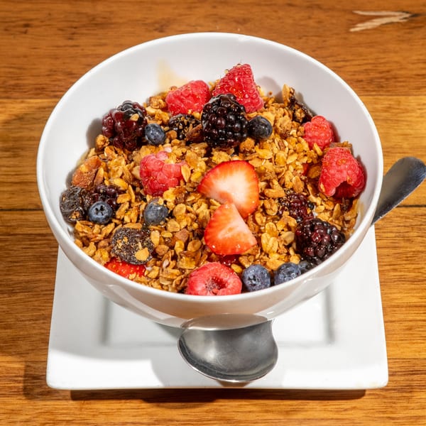 A white bowl of granola with fresh raspberries, blueberries, blackberries, and sliced strawberries.
