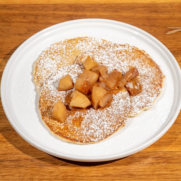 Café Muse pancakes topped with powdered sugar and caramelized apples on a white plate.
