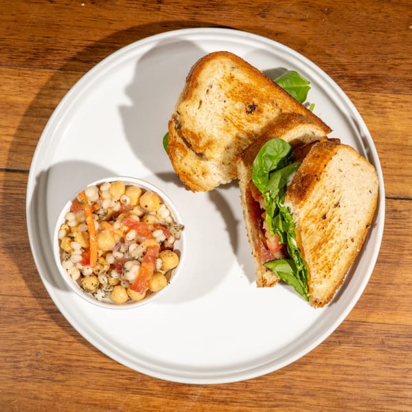 A toasted sandwich with spinach and tomatoes, served with a side of chickpea salad on a white plate.