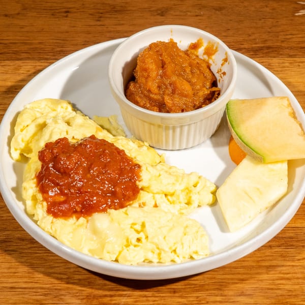 Scrambled eggs with red sauce, a side of fruit, and a bowl of orange jam.