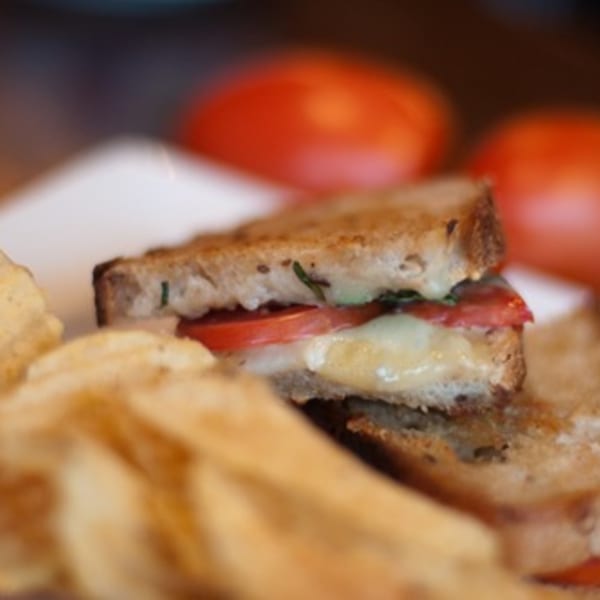 Grilled cheese sandwich with melted cheese and sliced tomatoes, served with potato chips.