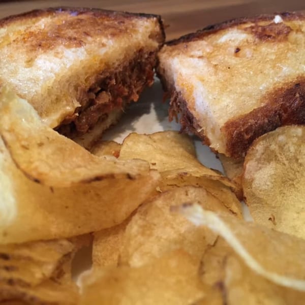 A grilled sandwich, cut in half to show its filling, served with a side of potato chips.