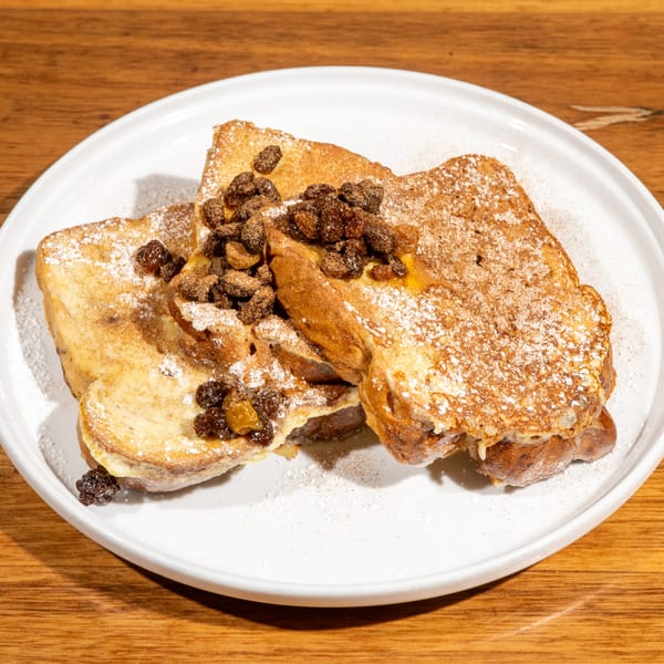 Café Muse's French toast, topped with powdered sugar, cinnamon, and raisins, on a white plate.