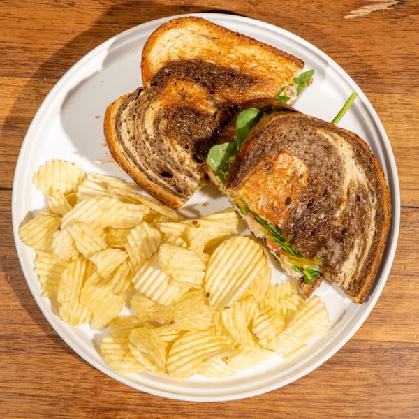 A Café Muse breakfast sandwich on marbled rye with chips, served on a white plate.
